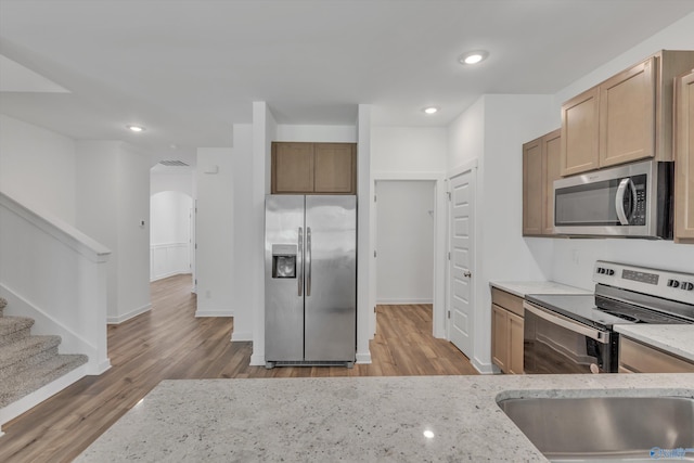 kitchen featuring light stone countertops, appliances with stainless steel finishes, sink, and light wood-type flooring