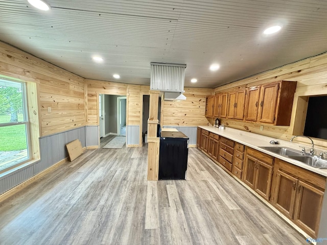 kitchen featuring a sink, light wood finished floors, brown cabinetry, and wood walls