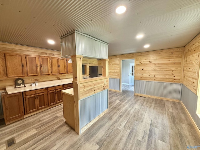 kitchen featuring light countertops, wood walls, brown cabinetry, and light wood-type flooring