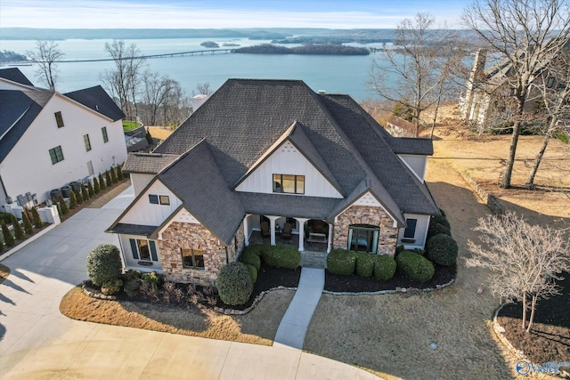 view of front of house featuring board and batten siding, a water view, roof with shingles, covered porch, and stone siding