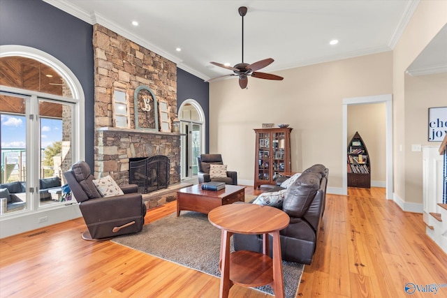 living area featuring crown molding, baseboards, a stone fireplace, light wood-style flooring, and a ceiling fan