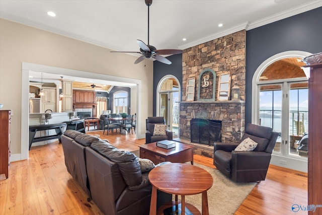 living area with ornamental molding, light wood-style floors, a stone fireplace, baseboards, and ceiling fan