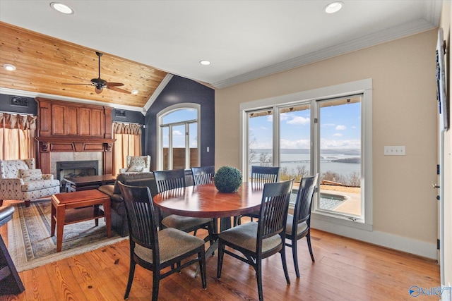 dining space with a ceiling fan, baseboards, a premium fireplace, light wood-style flooring, and ornamental molding