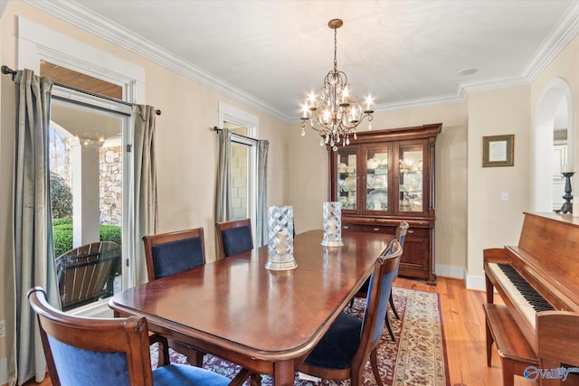 dining room featuring arched walkways, crown molding, light wood finished floors, baseboards, and a chandelier