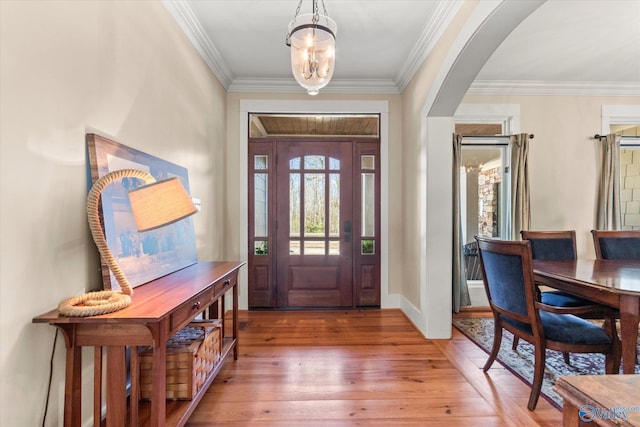 foyer entrance featuring baseboards, arched walkways, light wood-style flooring, and ornamental molding