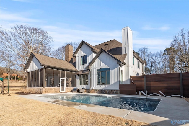 back of house with roof with shingles, board and batten siding, a sunroom, an outdoor pool, and a chimney