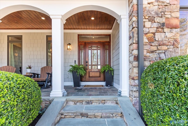 view of exterior entry with stone siding and covered porch