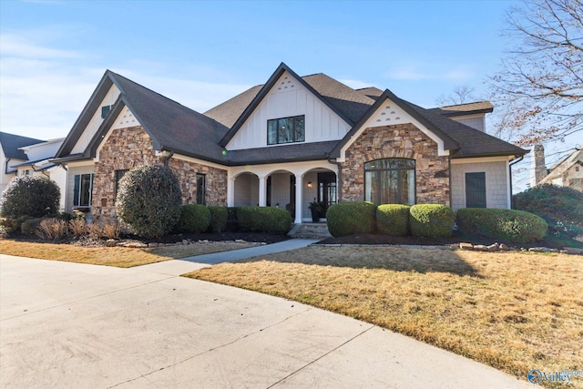 view of front facade featuring stone siding, board and batten siding, a front lawn, and roof with shingles