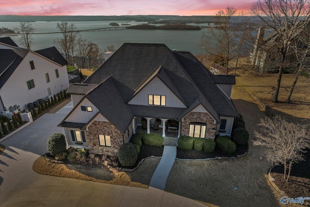 view of front of house with board and batten siding, a water view, stone siding, and roof with shingles