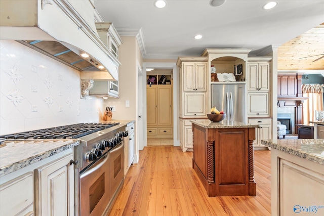 kitchen with cream cabinetry, ornamental molding, custom range hood, open shelves, and appliances with stainless steel finishes