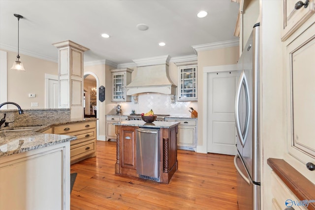 kitchen with custom exhaust hood, arched walkways, a sink, decorative backsplash, and appliances with stainless steel finishes