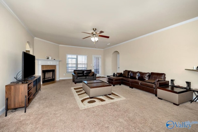 living area with ceiling fan, arched walkways, a tile fireplace, light carpet, and baseboards