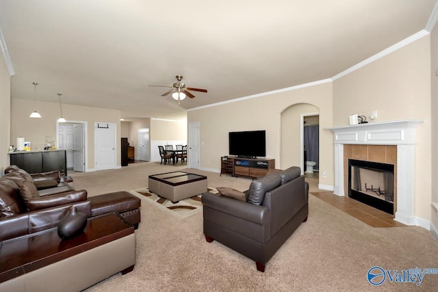 tiled living room with carpet floors, arched walkways, ornamental molding, a tile fireplace, and baseboards