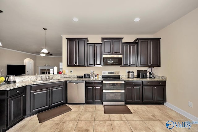 kitchen featuring arched walkways, ceiling fan, light stone counters, a sink, and appliances with stainless steel finishes