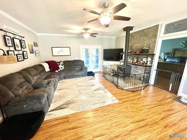 living room featuring a ceiling fan, ornamental molding, wood finished floors, and a wood stove