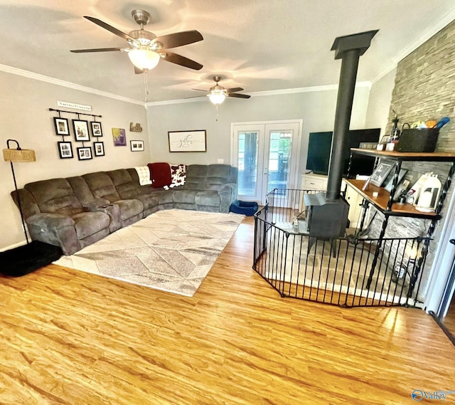 living room with crown molding, a ceiling fan, a wood stove, and wood finished floors
