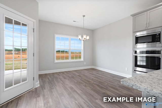 kitchen featuring a healthy amount of sunlight, a chandelier, pendant lighting, appliances with stainless steel finishes, and hardwood / wood-style flooring