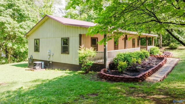 view of side of property featuring covered porch, central AC, and a yard