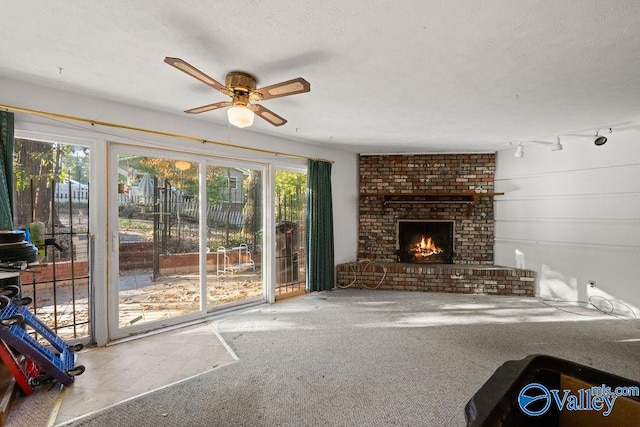 unfurnished living room with track lighting, ceiling fan, a textured ceiling, carpet flooring, and a brick fireplace