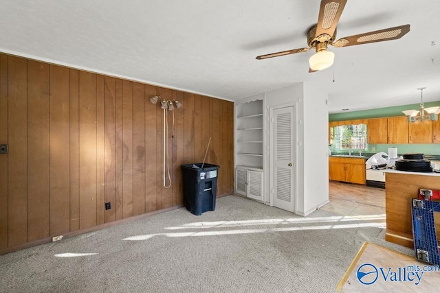 interior space featuring light carpet, sink, wooden walls, and ceiling fan with notable chandelier