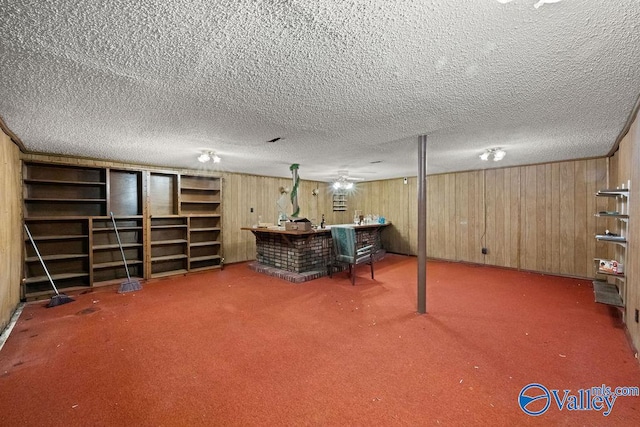 basement featuring wooden walls, a textured ceiling, and bar area