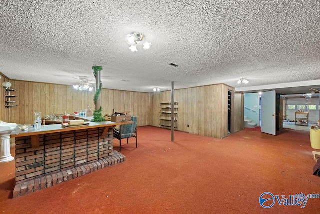 interior space with carpet, a textured ceiling, wooden walls, and ceiling fan