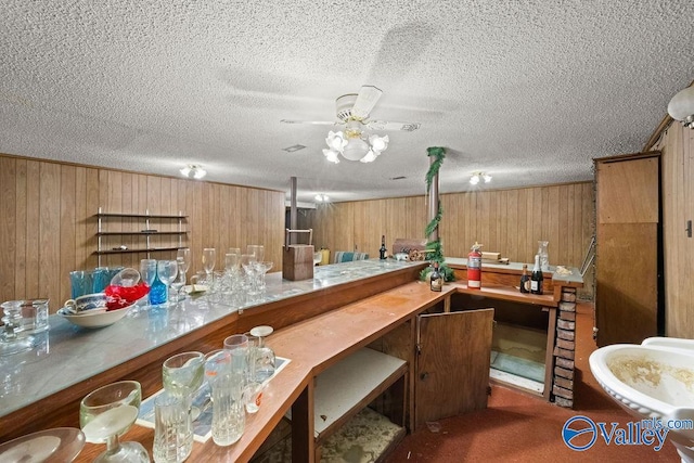 bar with ceiling fan, a textured ceiling, wooden walls, and dark carpet