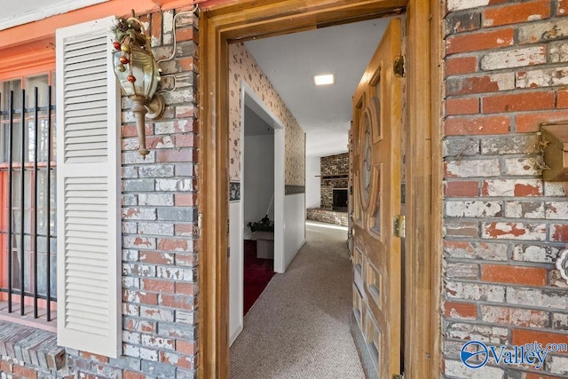 hallway featuring brick wall and dark colored carpet