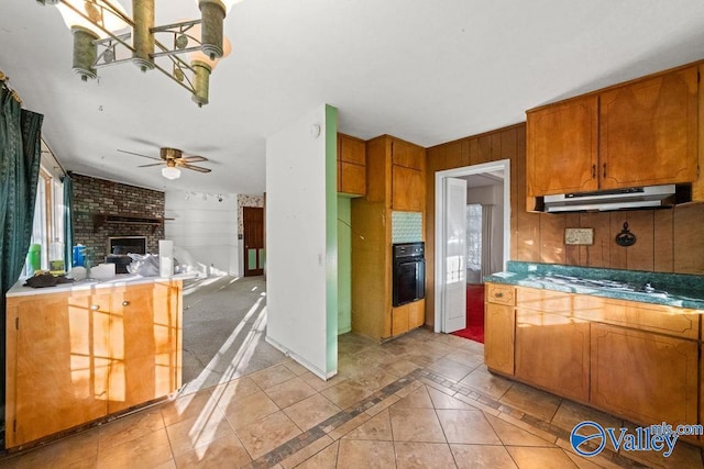 kitchen featuring stainless steel gas cooktop, oven, wooden walls, and ceiling fan