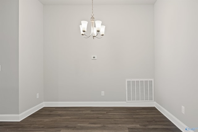 spare room featuring a chandelier, dark wood-style flooring, visible vents, and baseboards