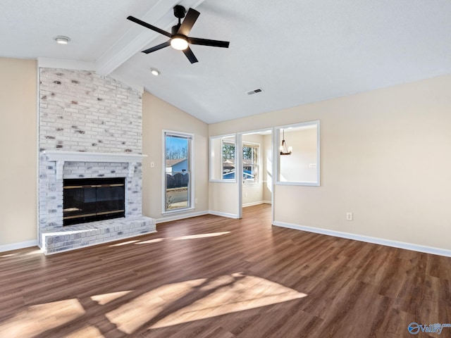 unfurnished living room with ceiling fan with notable chandelier, hardwood / wood-style floors, lofted ceiling with beams, and a brick fireplace