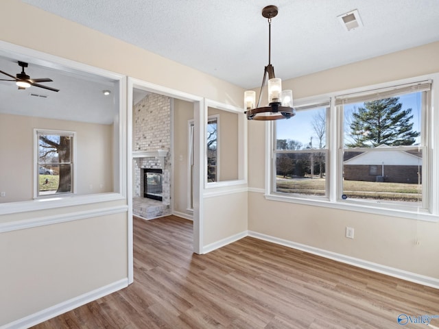 unfurnished dining area featuring wood-type flooring, a fireplace, vaulted ceiling, and a wealth of natural light