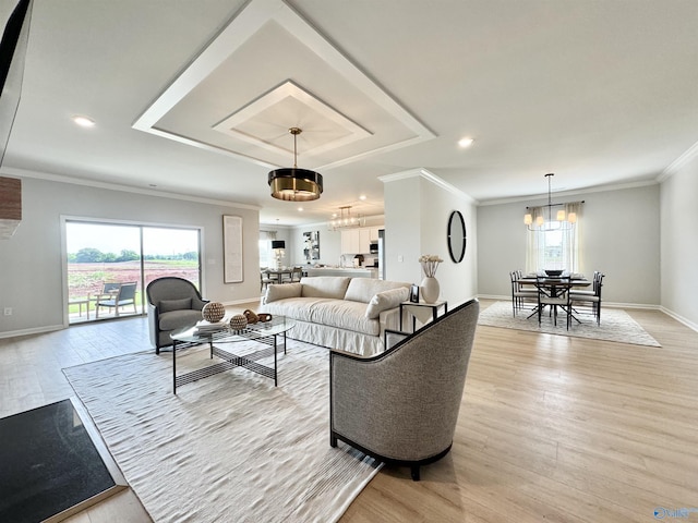 living room with an inviting chandelier, a tray ceiling, a wealth of natural light, and light wood finished floors