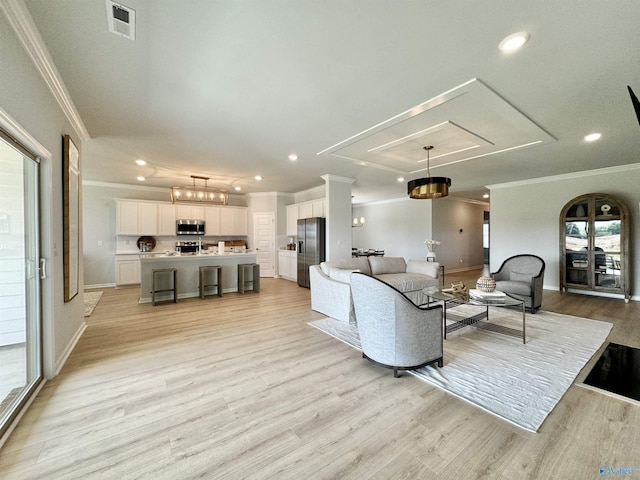 living room featuring visible vents, baseboards, attic access, ornamental molding, and light wood-style floors