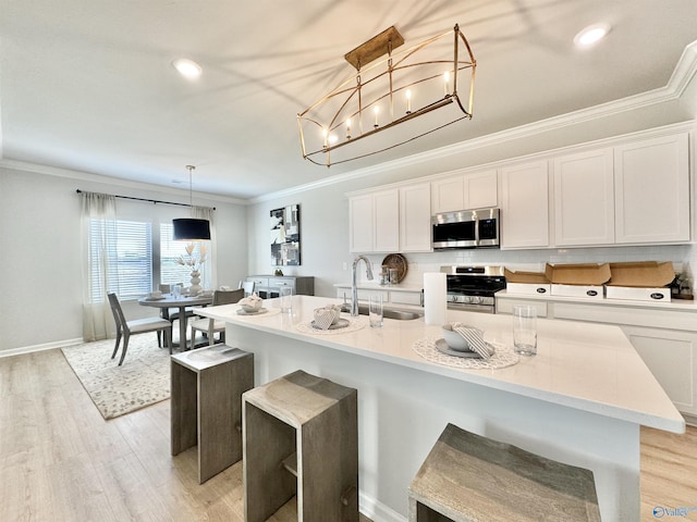 kitchen with a sink, light wood-style floors, appliances with stainless steel finishes, and ornamental molding