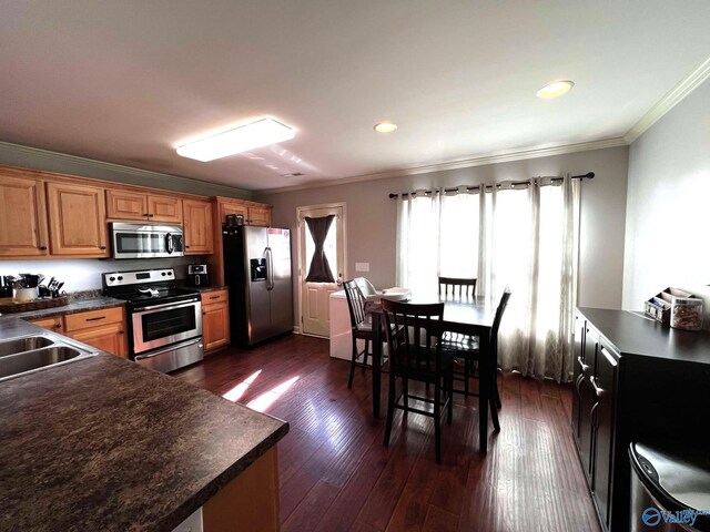 kitchen with brown cabinetry, dark countertops, dark wood-style floors, appliances with stainless steel finishes, and crown molding