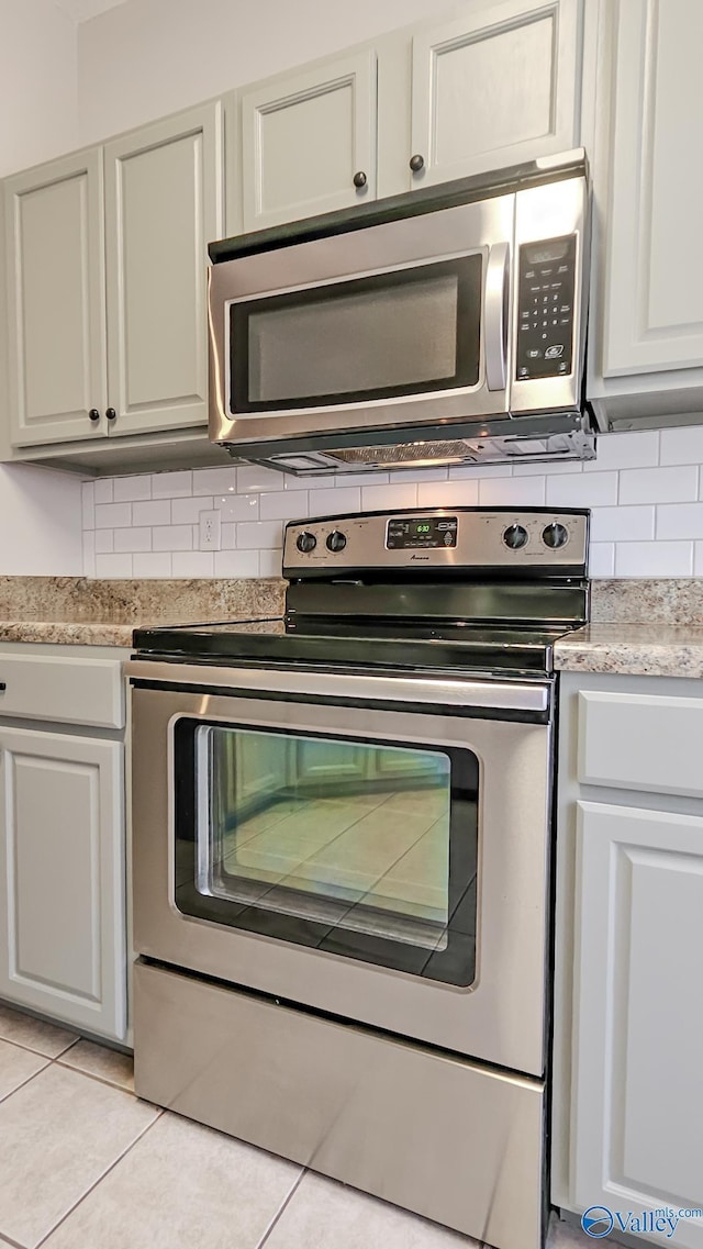 kitchen with white cabinets, light tile patterned floors, stainless steel appliances, and decorative backsplash