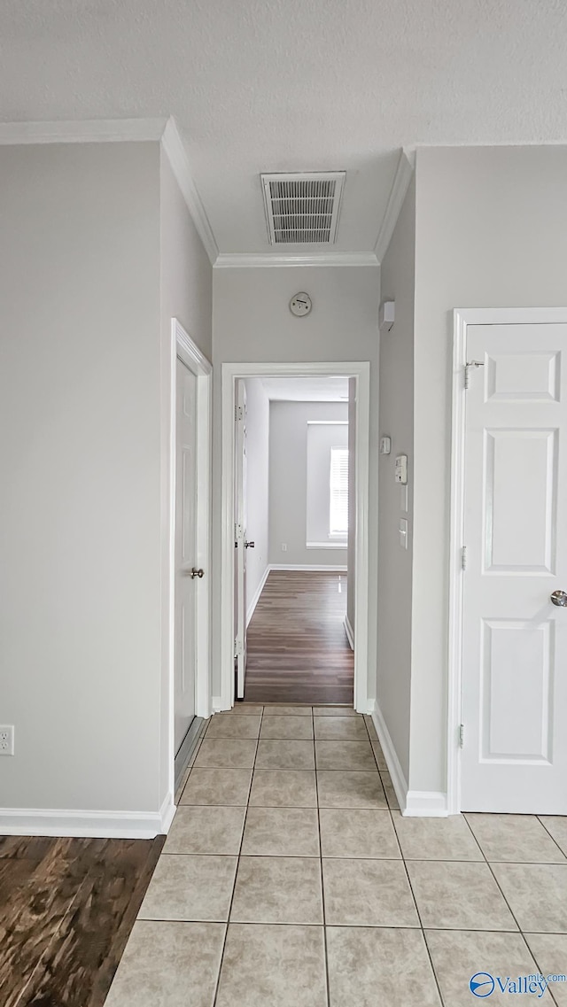 corridor featuring baseboards, visible vents, a textured ceiling, crown molding, and light tile patterned flooring