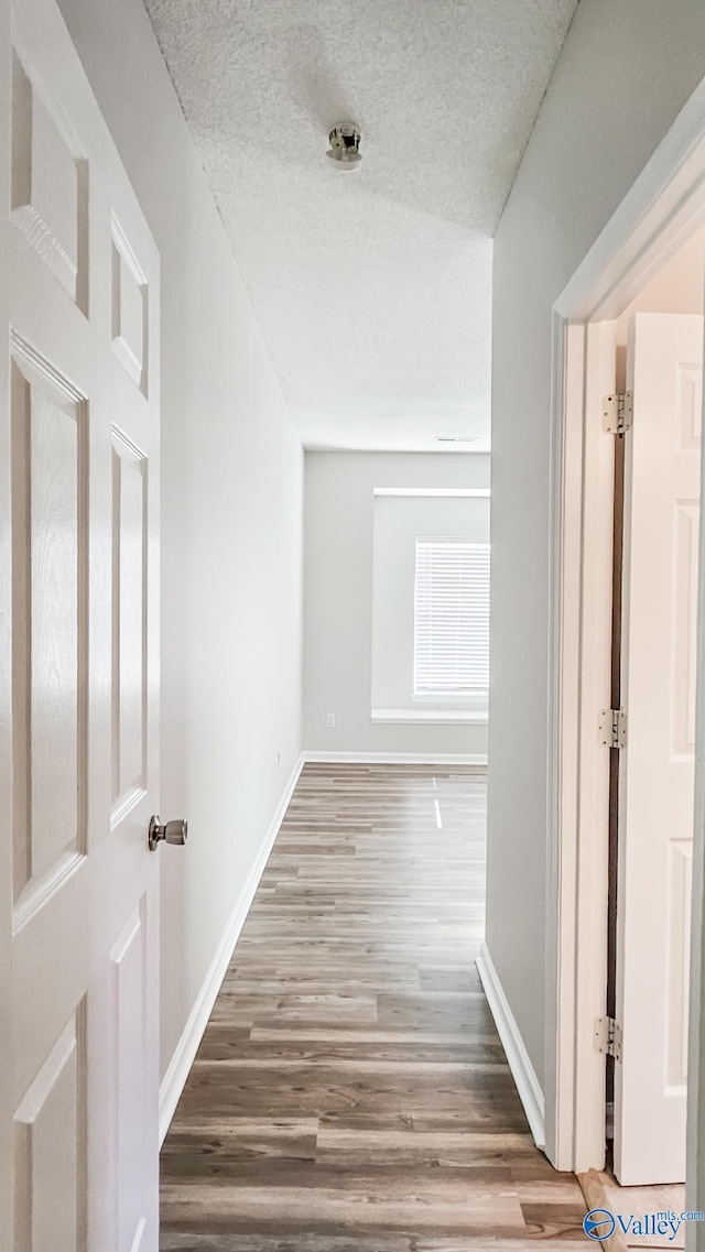 hall with a textured ceiling, baseboards, and wood finished floors