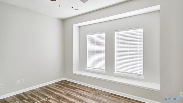 spare room featuring a wealth of natural light, baseboards, visible vents, and wood finished floors