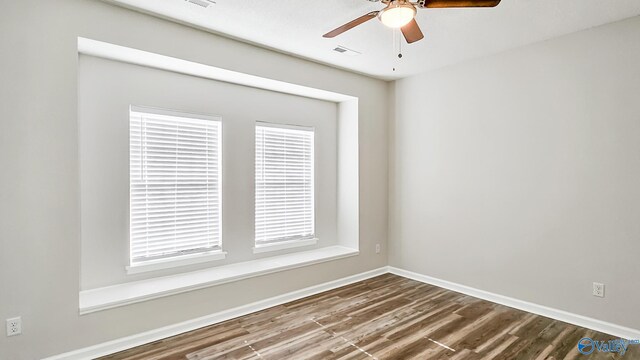 unfurnished room with visible vents, a healthy amount of sunlight, ceiling fan, wood finished floors, and baseboards