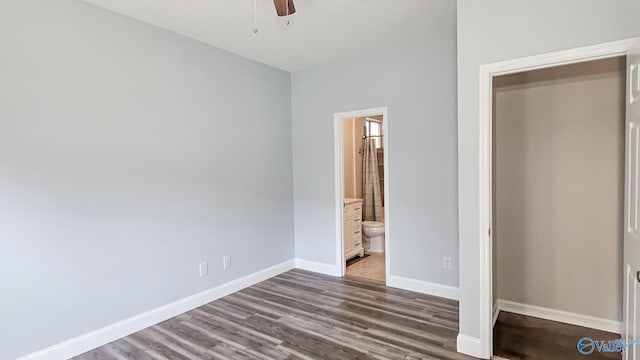 unfurnished bedroom with ensuite bath, wood finished floors, a ceiling fan, and baseboards