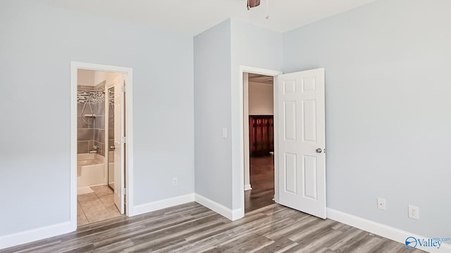 unfurnished bedroom featuring wood finished floors, connected bathroom, and baseboards