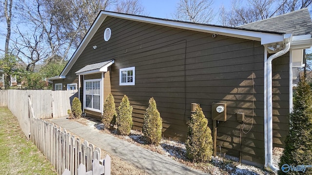 view of side of home featuring a shingled roof and fence