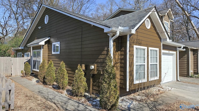 view of property exterior featuring a garage, concrete driveway, a shingled roof, and fence