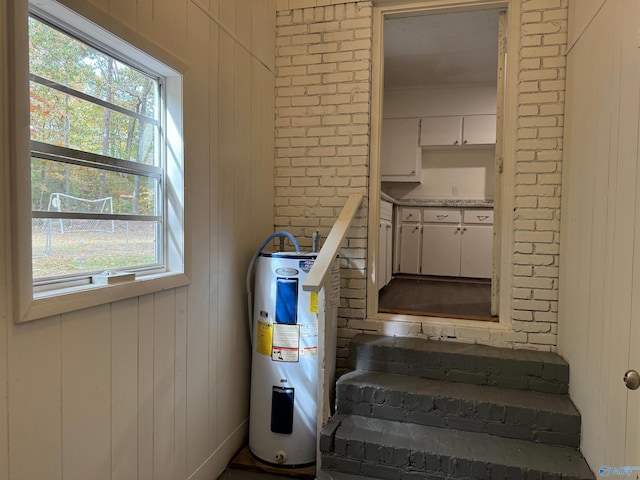 staircase with wood walls, electric water heater, and a healthy amount of sunlight