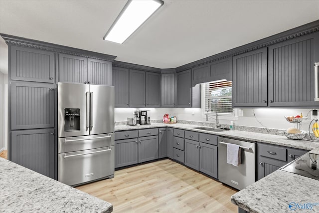 kitchen featuring sink, light wood-type flooring, gray cabinetry, stainless steel appliances, and light stone countertops