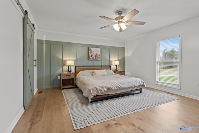 bedroom with light wood-type flooring, crown molding, ceiling fan, and a barn door