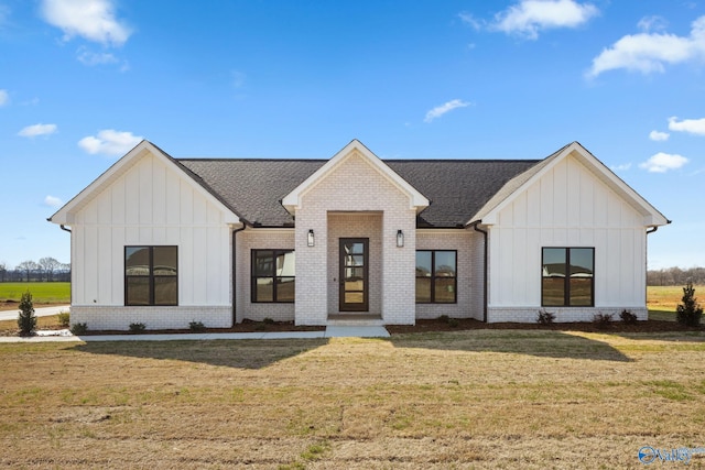 modern farmhouse style home with board and batten siding, brick siding, a front yard, and roof with shingles