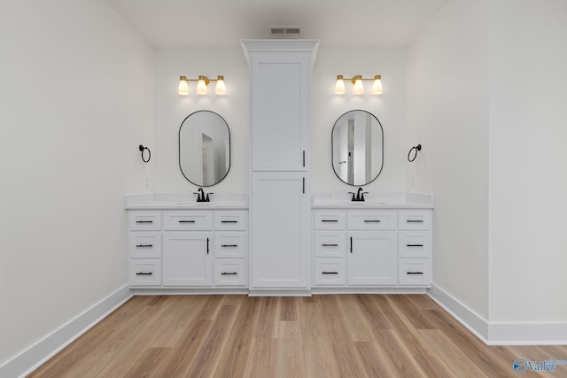 full bath featuring baseboards, a sink, wood finished floors, and two vanities